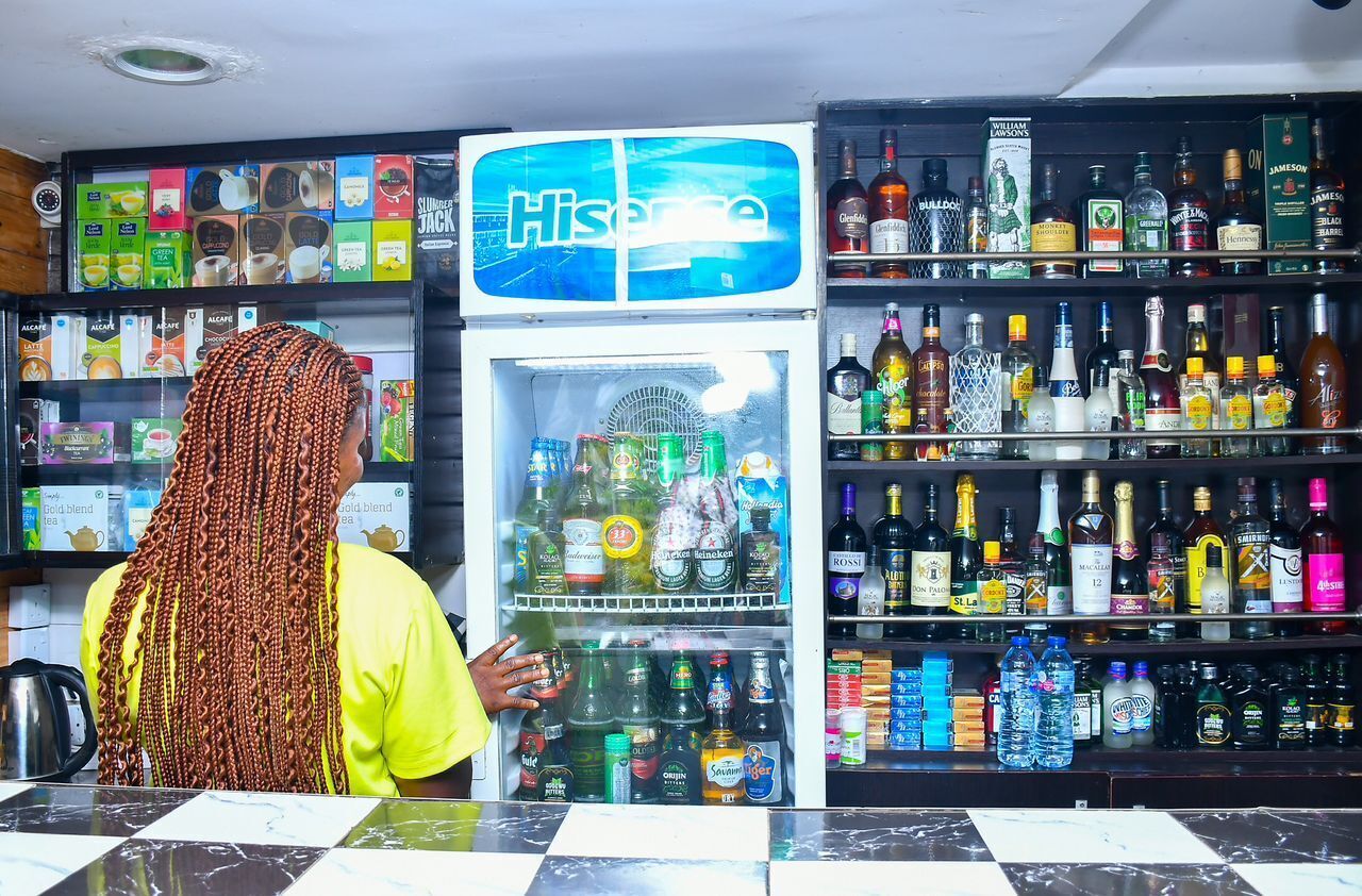 A person at a counter with a beverage dispenser and shelves stocked with various drinks.
