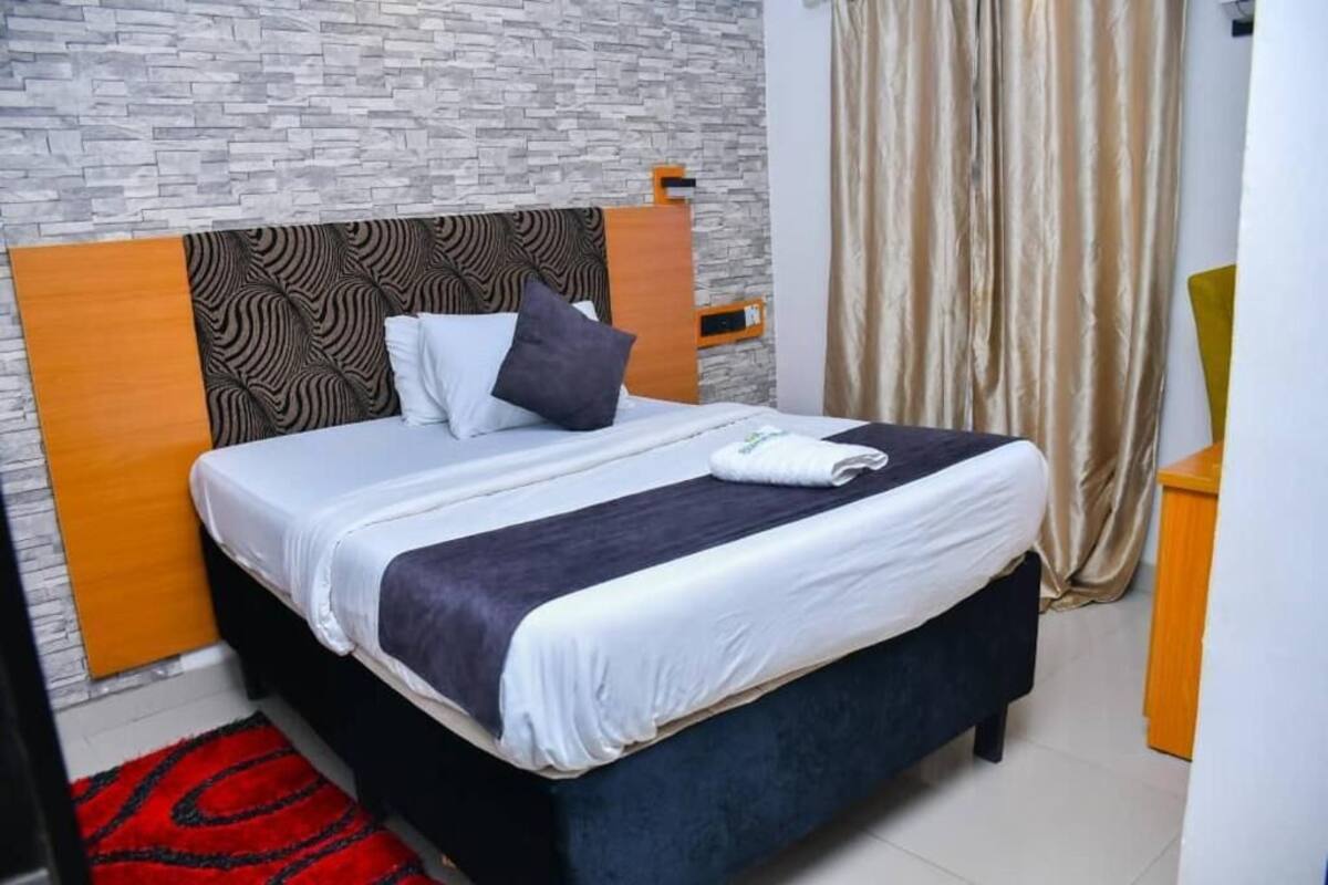A neatly made bed with a patterned headboard, a red rug, and a wooden nightstand.