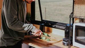 A person cutting vegetables on a wooden cutting board in a kitchen with a coffee machine and a microwave. - Tiny Boorowa by Tiny Away (Boorowa)