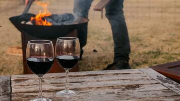 Two wine glasses on a rustic wooden table with a fire pit in the background.