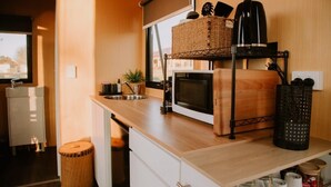 A compact kitchen with a microwave, toaster, and wicker baskets on a wooden countertop. - Tiny Boorowa by Tiny Away (Boorowa)