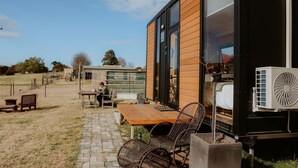 A modern mobile home with a wooden exterior, large windows, and a patio area with outdoor furniture. - Tiny Boorowa by Tiny Away (Boorowa)