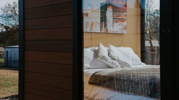 A bedroom with a bed, pillows, and a large window. - Tiny Boorowa by Tiny Away (Boorowa)