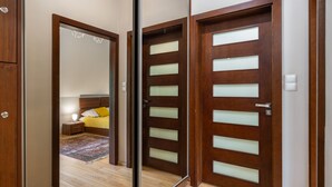 Une porte en bois avec des panneaux de verre dépoli, un lit visible avec un oreiller jaune, et une table de chevet avec une lampe dans la pièce adjacente.