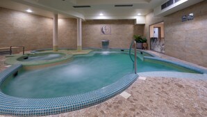Une piscine intérieure avec un sol et des murs carrelés, une fontaine centrale et une porte donnant sur une autre pièce.