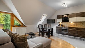 Un appartement moderne de style « loft », comprenant un coin repas, une cuisine et une grande fenêtre donnant sur un espace verdoyant.