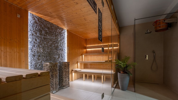 Un sauna avec des bancs en bois, un mur en pierre et une cloison en verre.