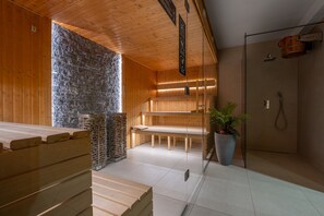 A sauna with wooden benches, a stone wall, and a glass partition. - RentPlanet - Gorące Źródła (Zakopane)