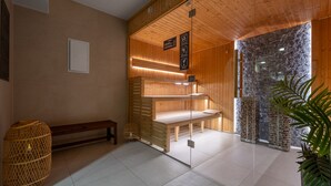 Un sauna avec des bancs en bois, un banc avec une serviette, un panier en osier et un mur en pierre.