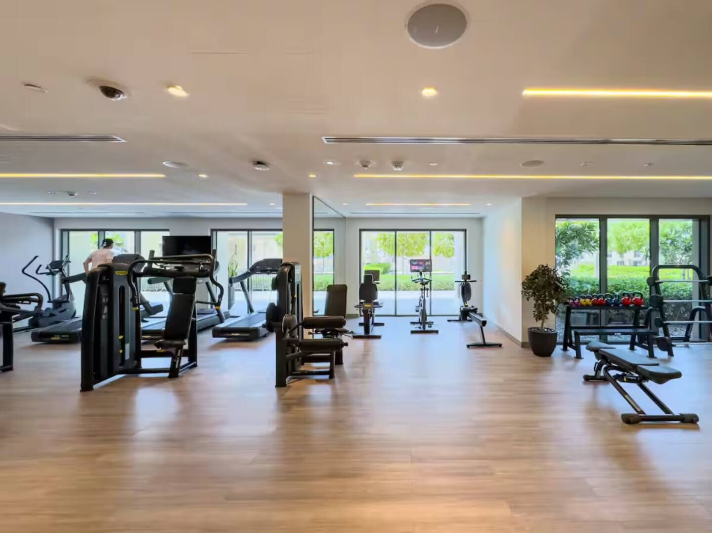 A spacious gym with various exercise equipment, large windows, and a clean, modern design.