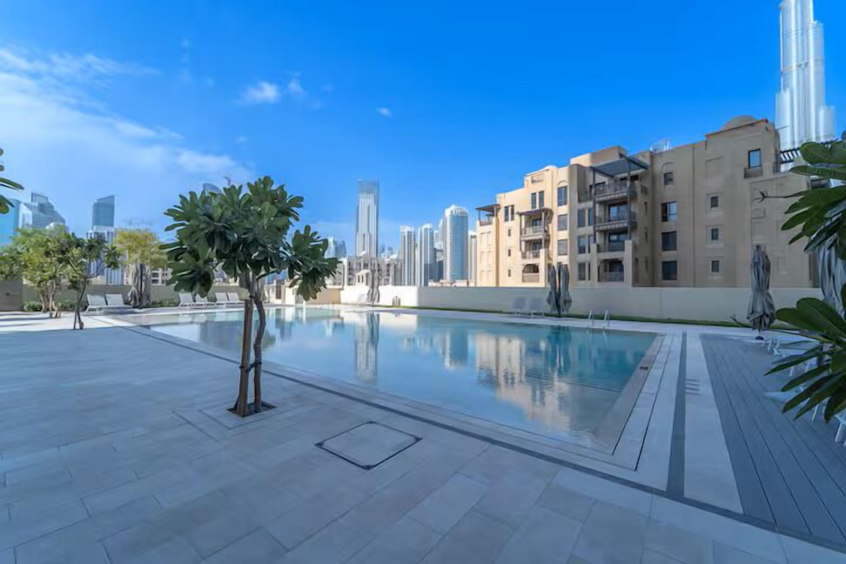 Un quartier résidentiel moderne doté d’une piscine, de palmiers et, en arrière-plan, de bâtiments de grande hauteur.