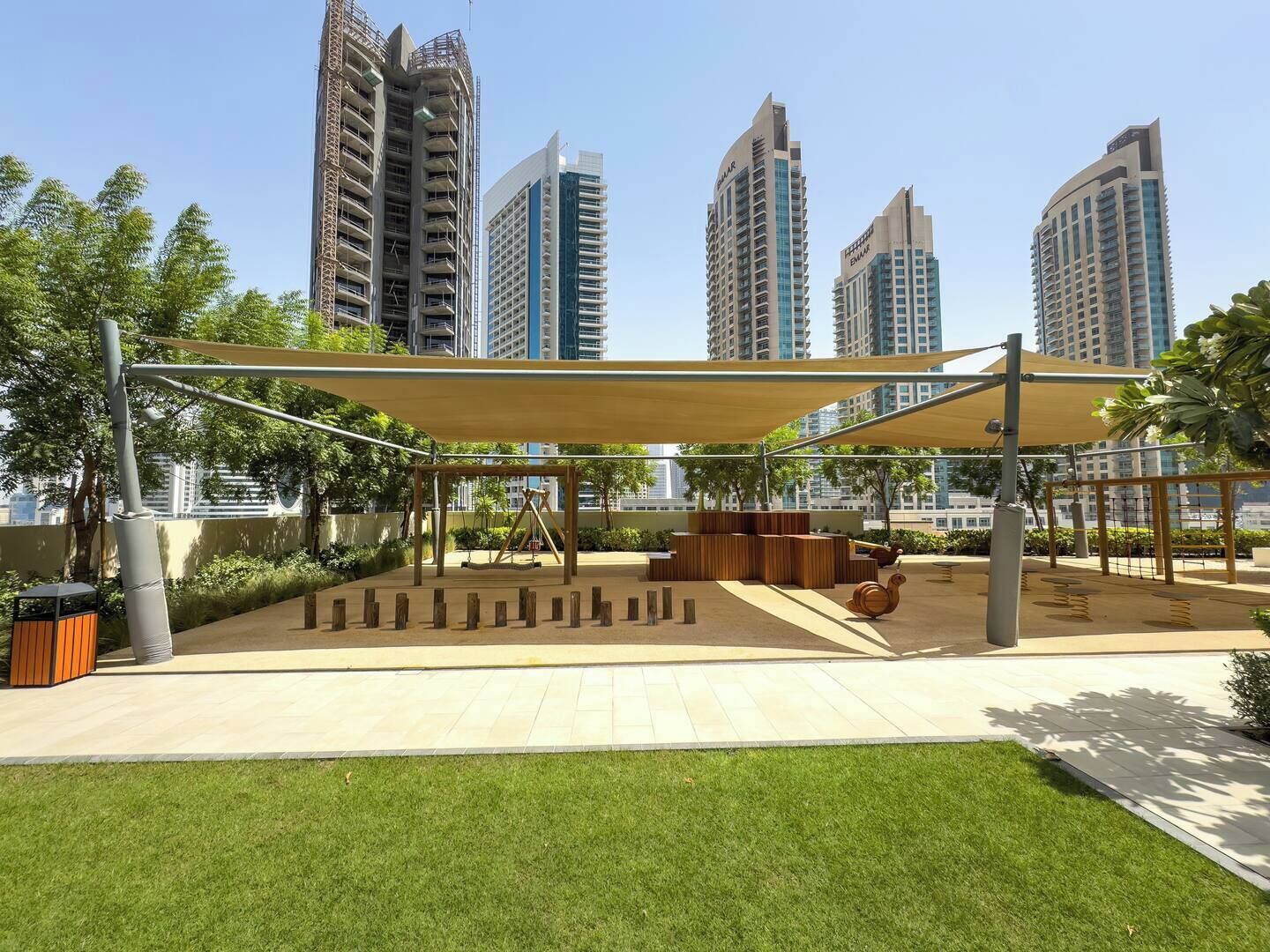 An outdoor park area with a swing set, seating, and a shaded canopy.
