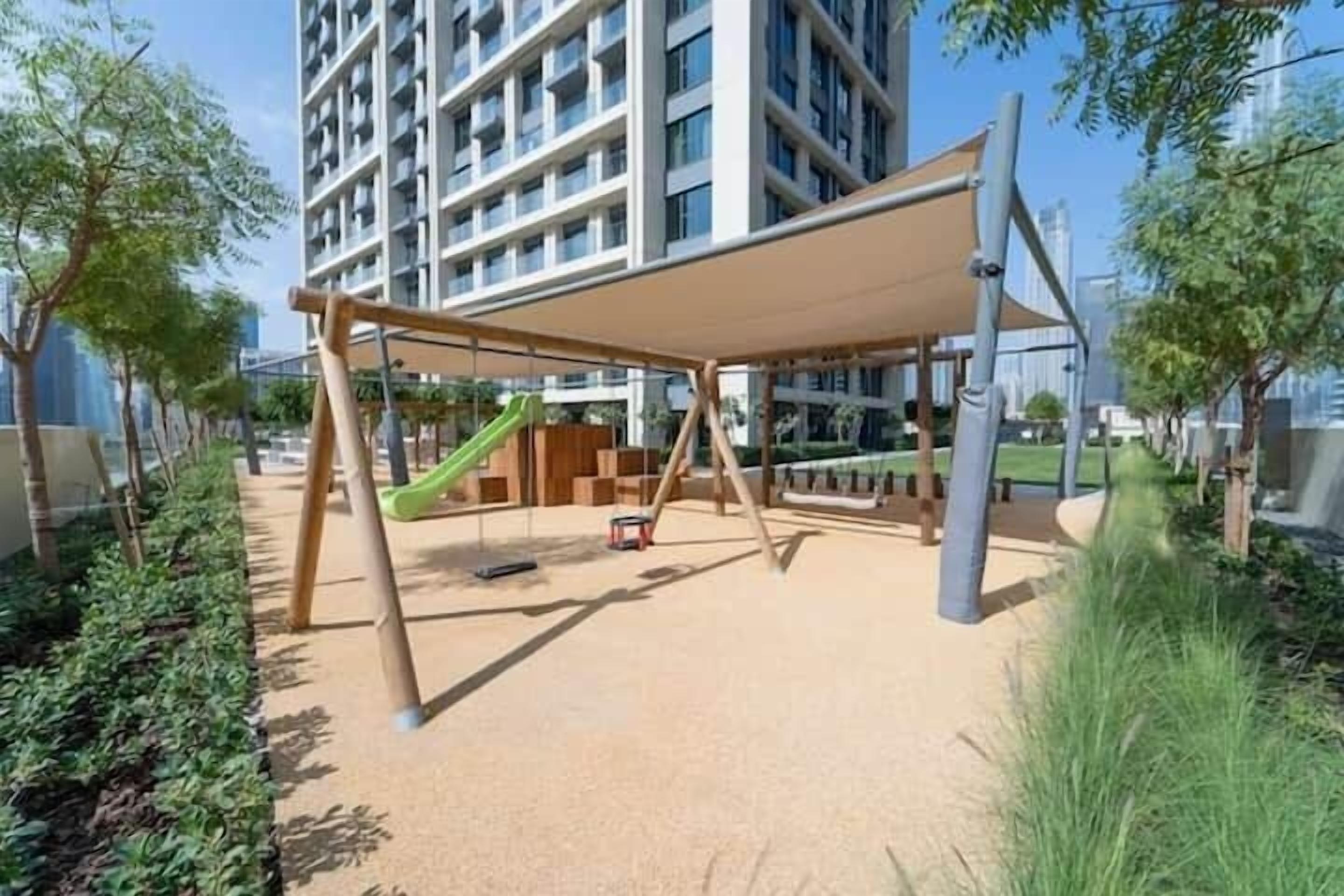 Ein Spielplatz mit Rutsche und Schaukeln, umgeben von einem Gebäude und Bäumen.