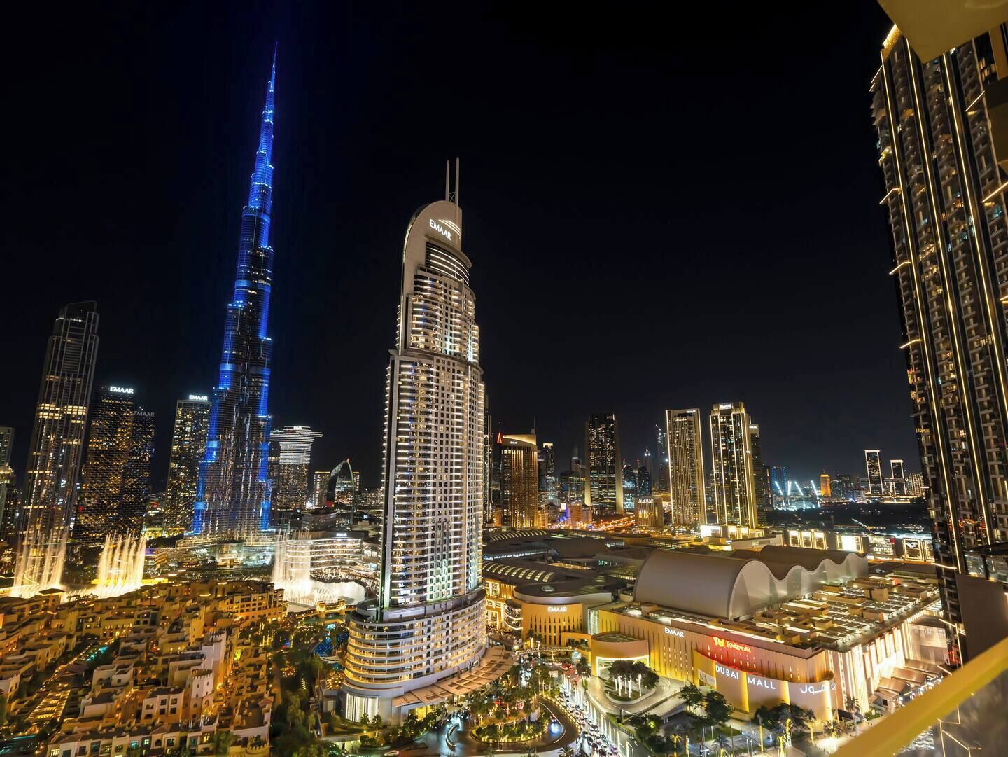 Un paisaje urbano nocturno con imponentes rascacielos, incluyendo un distintivo rascacielos curvo y el Burj Khalifa.