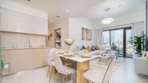A modern kitchen with white cabinets, a dining table set for four, and a living area with a sofa and a large window. - Vogue| in Heart of Downtown with Burj Khalifa view (Dubai)