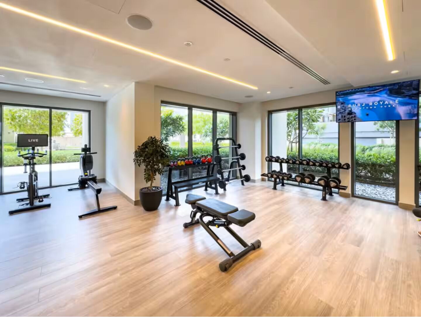 A modern gym with exercise equipment, large windows, and a TV screen.