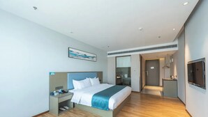 Moderni hotellihuone, jossa on suuri sänky, yöpöytä, televisio ja erillinen vaatehuone.