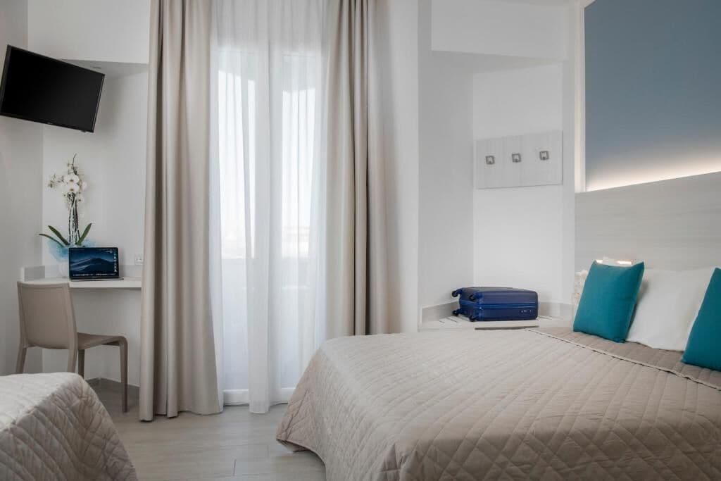 Habitación de hotel con dos camas, un escritorio con una computadora portátil, un televisor montado en la pared y una ventana con cortinas.