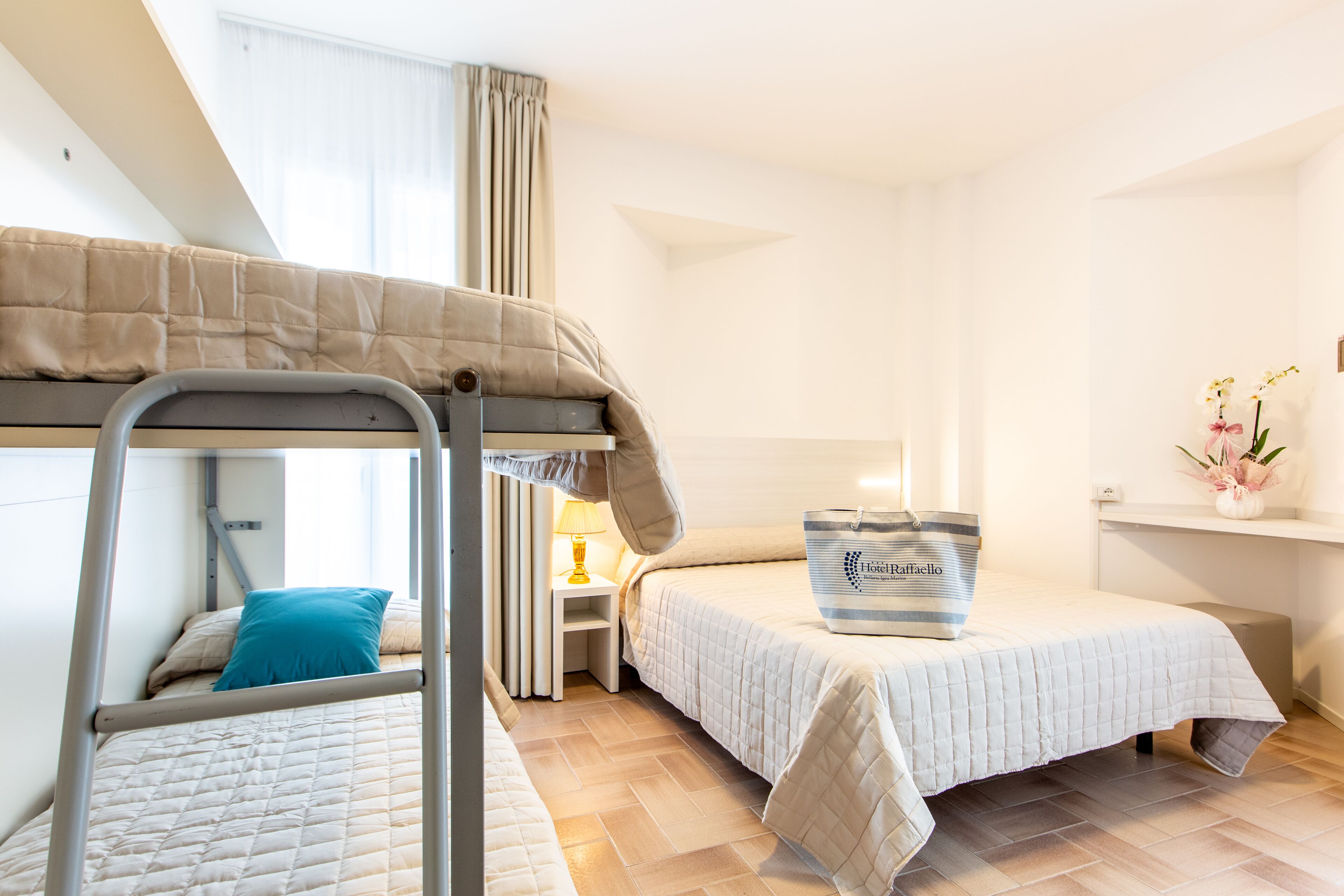 Una habitación de hotel con literas, una cama individual, una mesita de noche con una lámpara, un jarrón decorativo y un bolso sobre la cama.