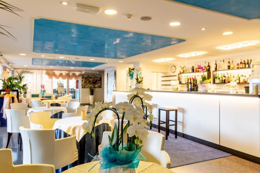 Un hall d’hôtel avec des chaises blanches, un coin bar avec des bouteilles et un plafond orné d’un motif bleu.