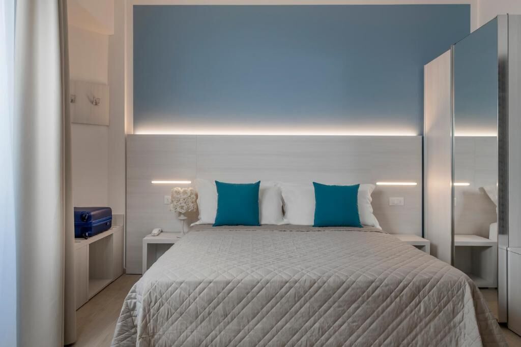 Un dormitorio moderno con una cama grande, dos almohadas, una mesita de noche y un pequeño mueble auxiliar.