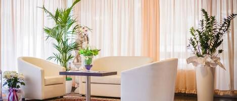 A modern living room with a white sofa, two armchairs, a coffee table, and decorative plants.