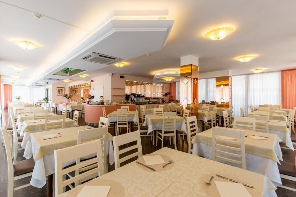 Un comedor espacioso con varias mesas y sillas, una zona de bar central, y un techo bien iluminado con luces empotradas.