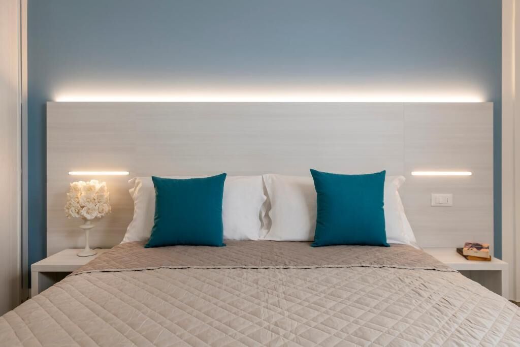 Een net opgemaakt bed met een gewatteerde hoes, twee kussens en een nachtkastje met een lamp en een boek.