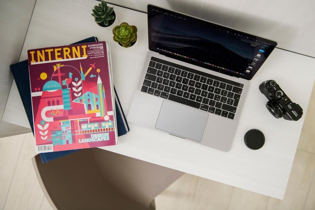 Un bureau avec un ordinateur portable, un magazine intitulé « PAYSAGES DU DESIGN INTERNATIONAL » et deux petites plantes en pot.