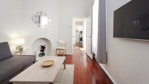 A modern living room with a sofa, a table, and a decorative mirror. A hallway leads to a laundry area.