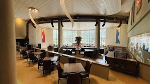 Un restaurant spacieux avec de hauts plafonds et de grandes fenêtres, comprenant un bar central et plusieurs espaces pour s’asseoir.