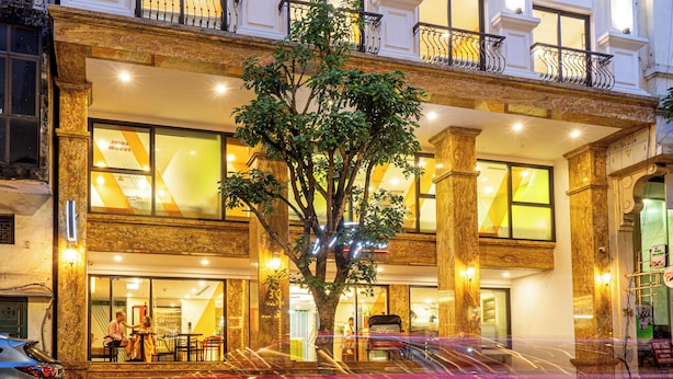 A hotel with a large tree in front, a balcony with iron railings, and a bright interior. - Wilque Hotel Hanoi (Hanoi)