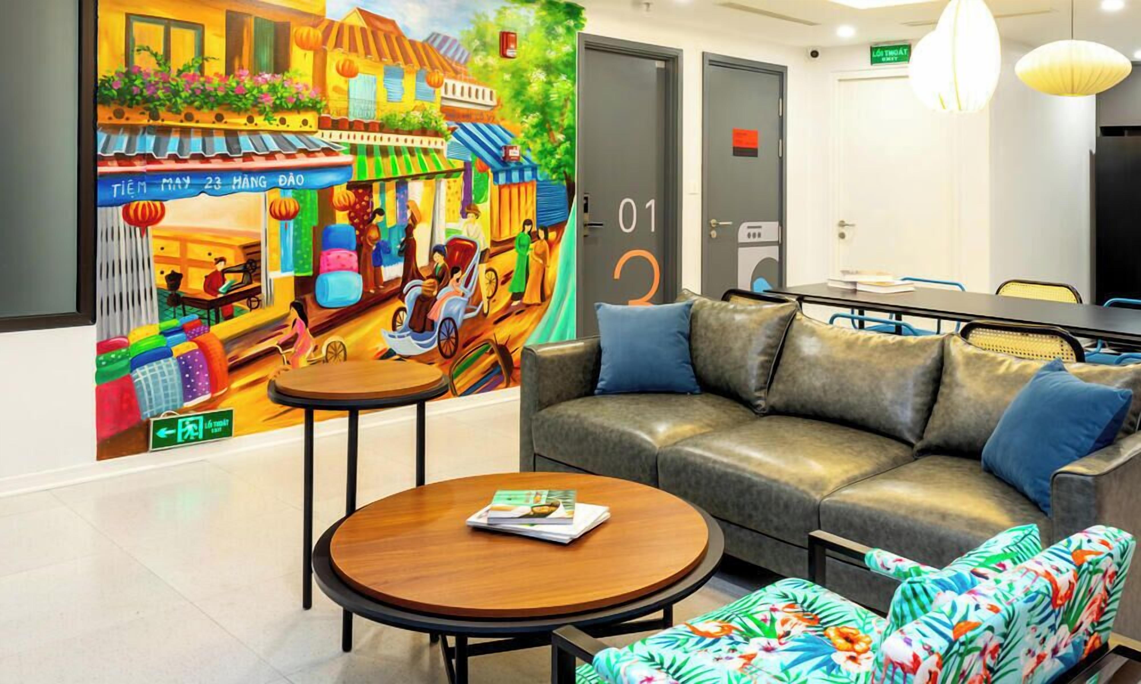 A hotel lobby with a colorful mural, a leather sofa, a round wooden table, and a patterned armchair.