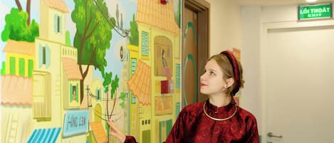 A person in a red garment pointing at a colorful mural depicting buildings and trees.