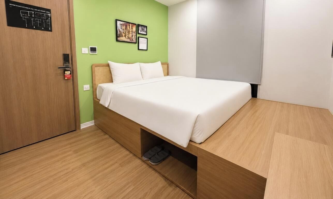 A modern hotel room with a wooden bed, green walls, and a visible evacuation plan on the door.