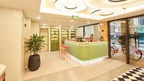 A modern bar area with a green counter, two orange bar stools, and a large potted plant. - Wilque Hotel Hanoi (Hanoi)