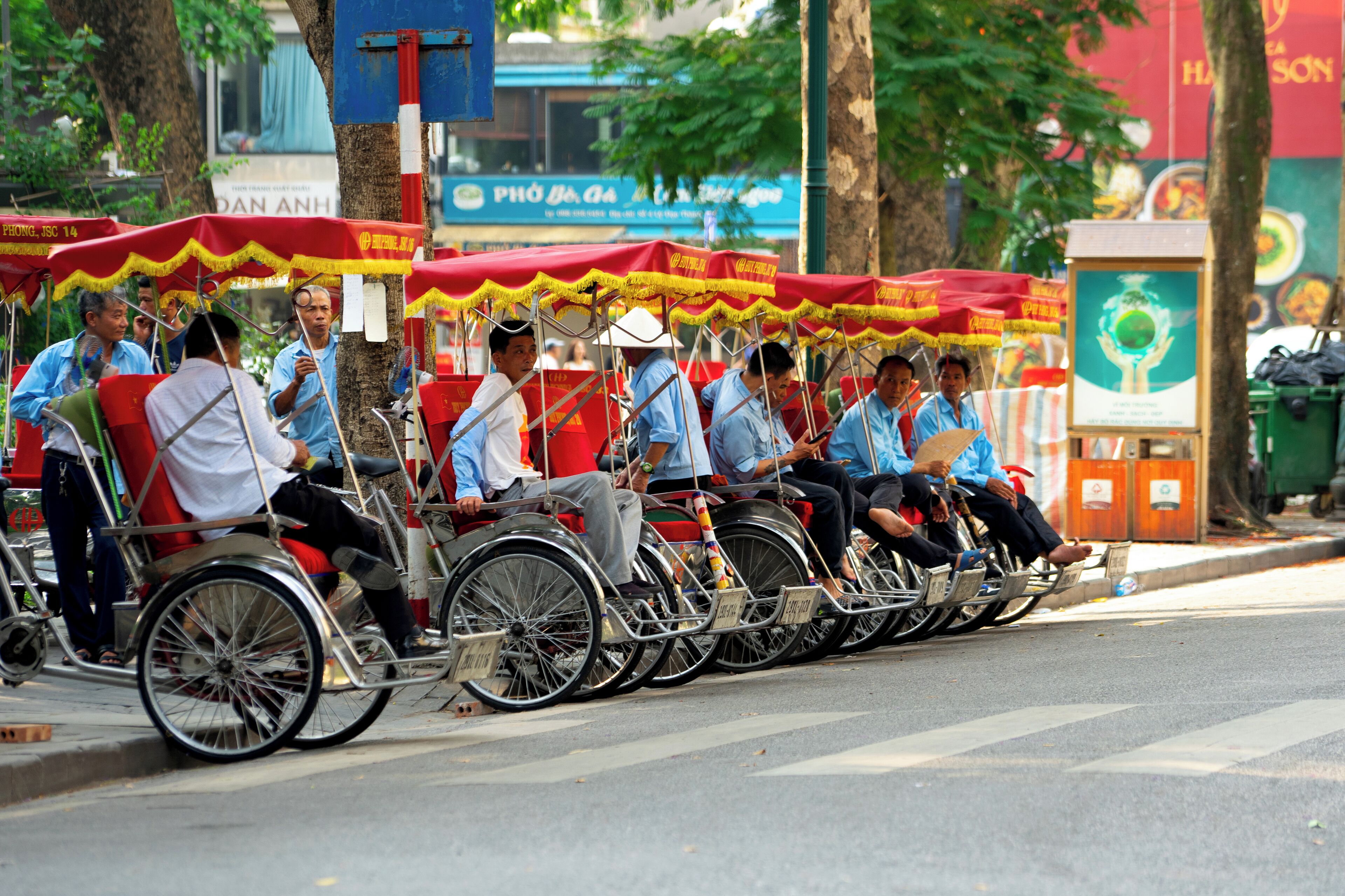 A line of rickshaws with passengers, parked on a street.