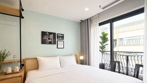 A hotel room with a bed, a nightstand, a potted plant, a window with a view of buildings, and framed pictures on the wall. - Wilque Hotel Hanoi (Hanoi)