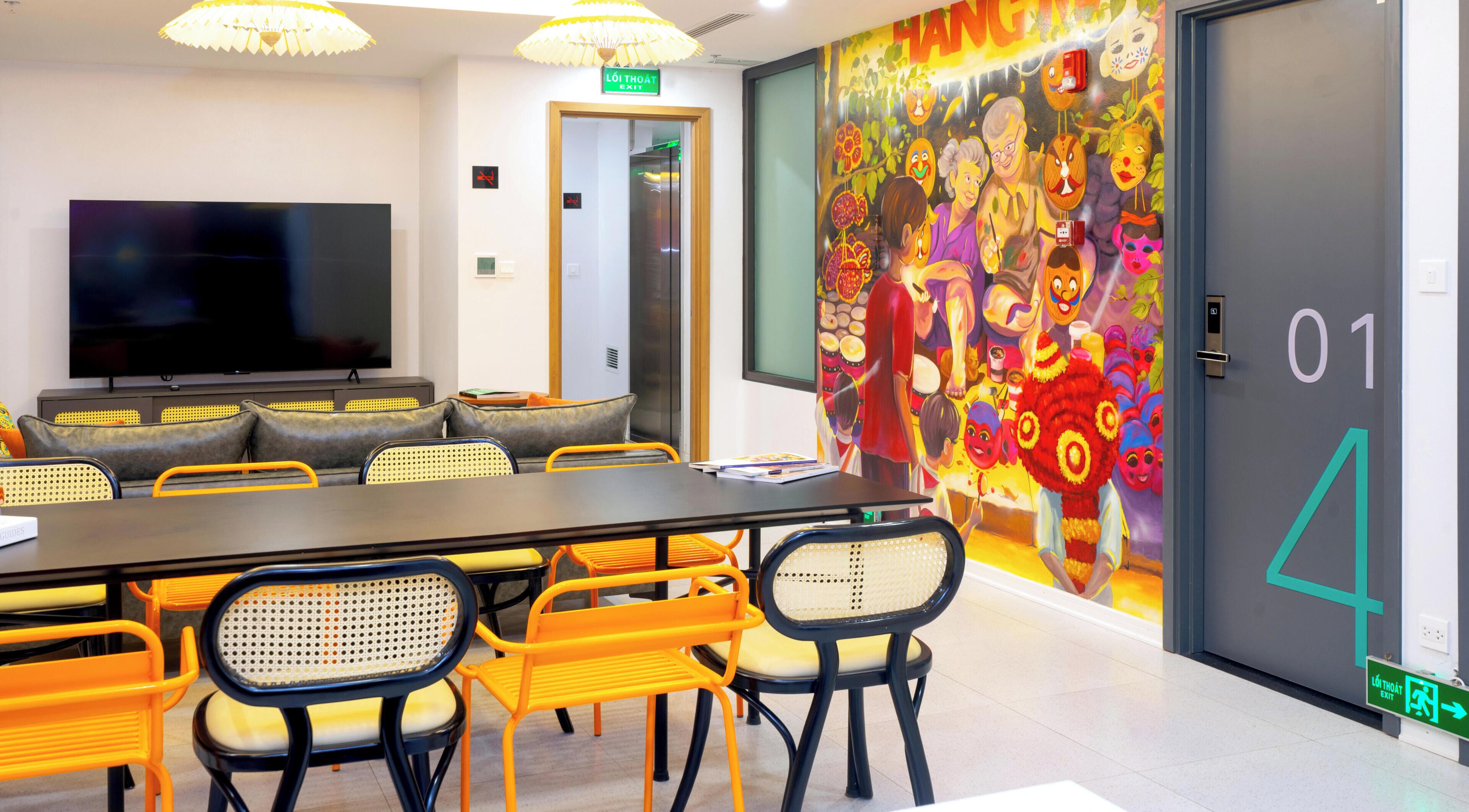 Une salle de conférence équipée d’un grand téléviseur à écran plat, d’une longue table avec des chaises et d’une fresque colorée sur le mur.