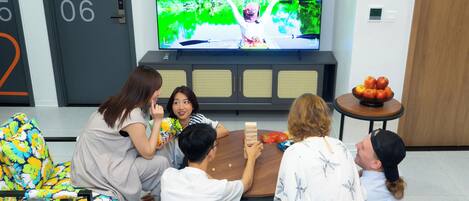 A group of people playing a board game in a modern living room with a television displaying a nature scene.