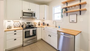 A modern kitchen with white cabinets, stainless steel appliances, a wooden countertop, and a built-in dishwasher. - Charming private house sleeps 4 with a large fenced yard, fast WiFi, smart TVs, and ample parking—near the Heights & Downtown. Features a primary king bed for a comfortable stay. (Houston)