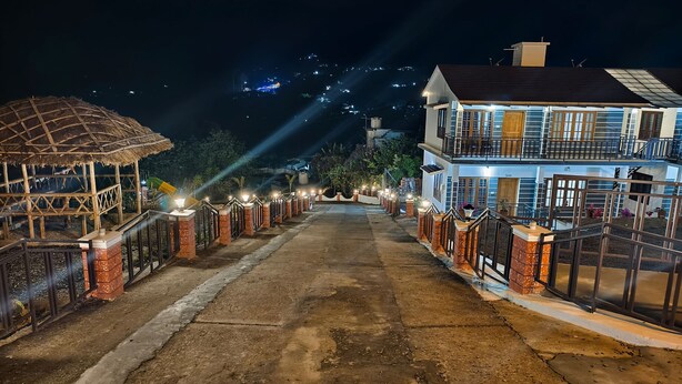 A two-story building with a balcony, a thatched-roof structure, and a paved pathway leading to the entrance. - Moon Wings Mountain Resort (Devikolam)