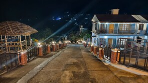 A two-story building with a balcony, a thatched-roof structure, and a paved pathway leading to the entrance. - Moon Wings Mountain Resort (Devikolam)