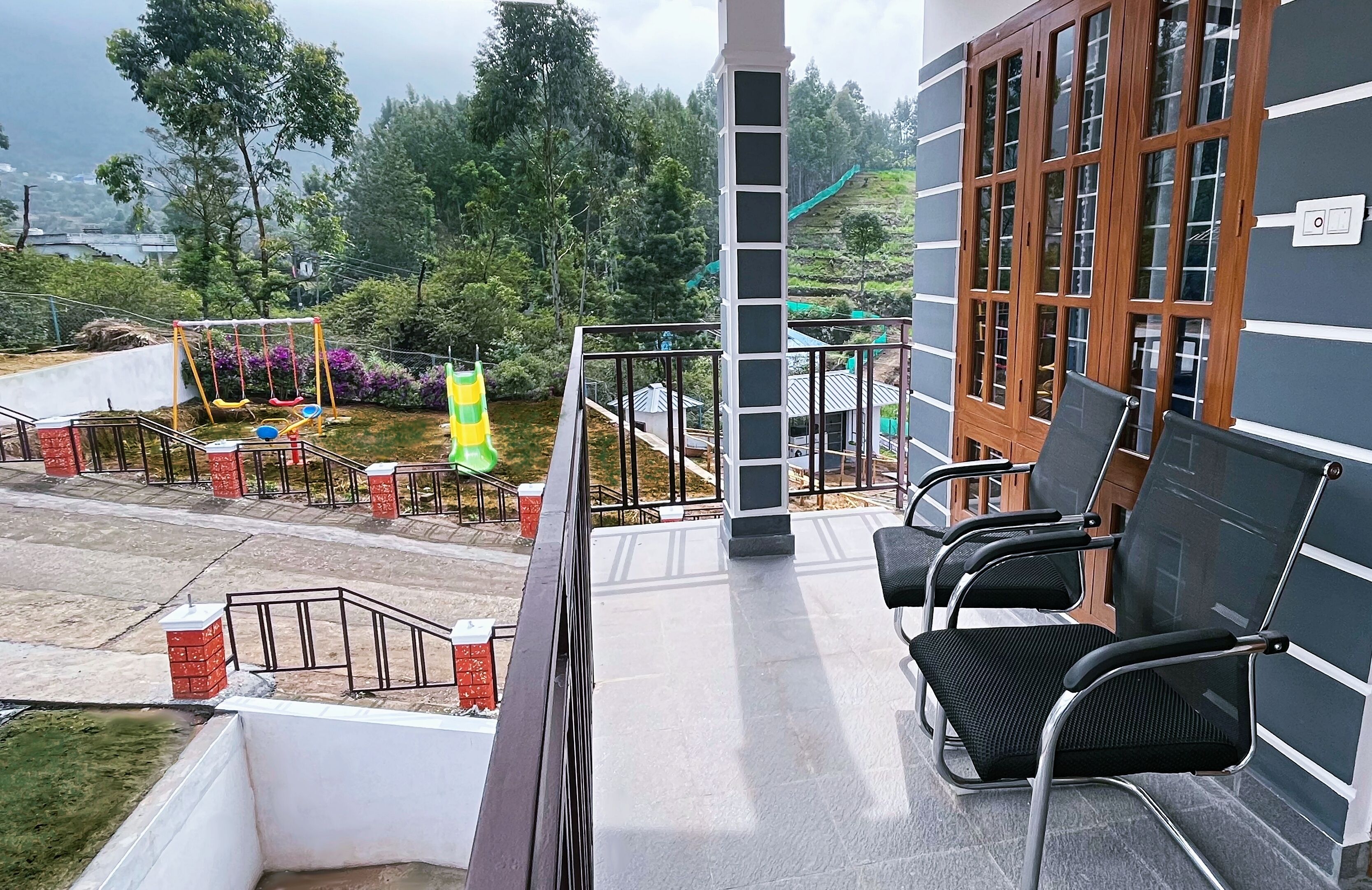 A balcony with black chairs, a swing set, and a view of a green landscape.