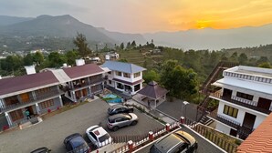 A multi-story building with a courtyard, cars parked in front, and a view of distant mountains. - Moon Wings Mountain Resort (Devikolam)
