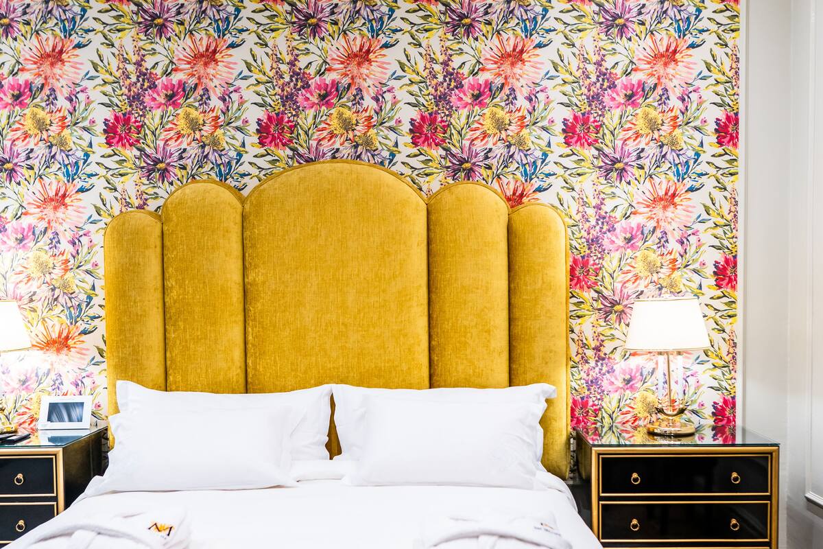 Ein ordentlich bezogenes Bett mit weißen Leinen, ein Kopfschild mit Blumenmuster und eine dekorative Rose darauf.