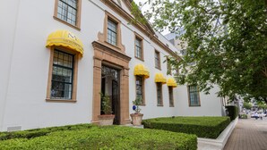 A white building with yellow awnings and a well-maintained hedge.