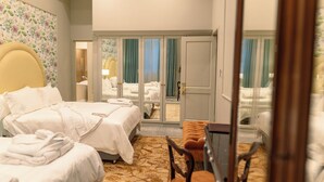 A hotel room with two beds, a sitting area, and a view through a glass door.