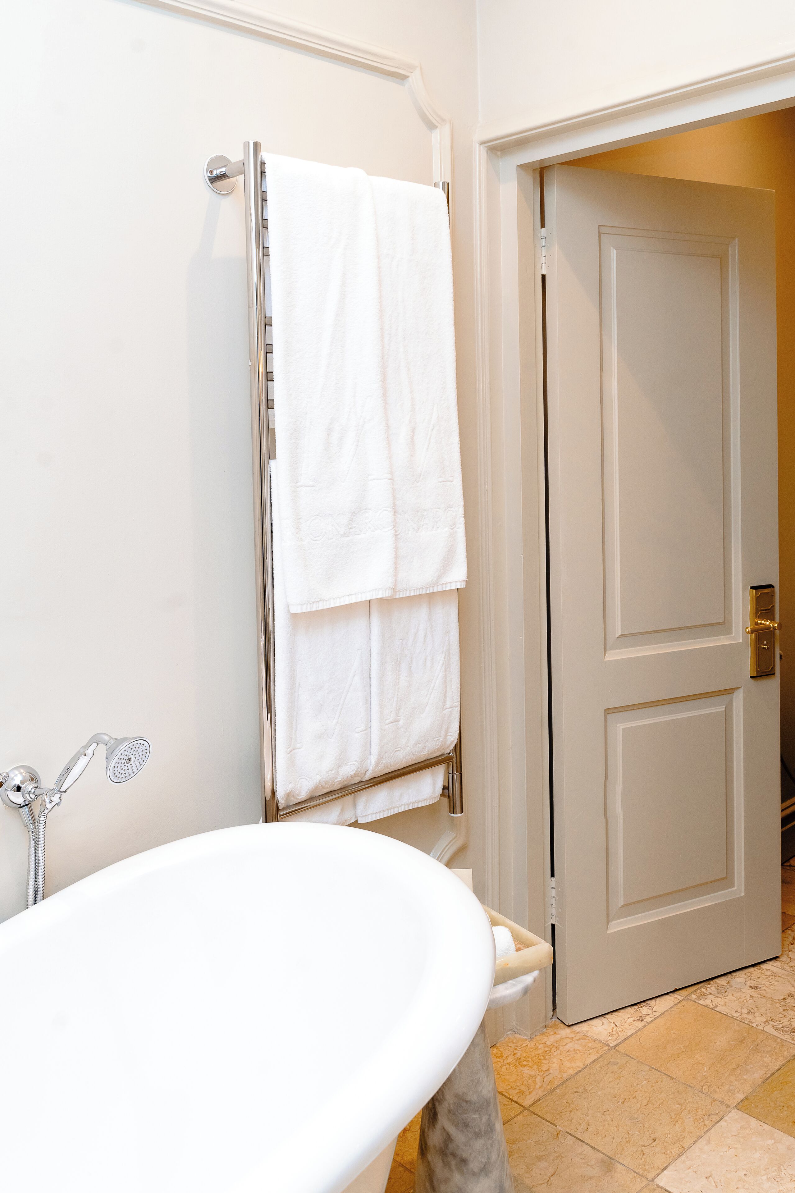 A bathroom with a white bathtub, a towel rack with two white towels, and a closed door.