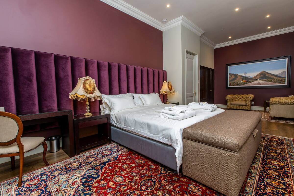 Ein Schlafzimmer mit einem großen Bett, einem Nachttisch, einem Sessel, einer Bank und einem großen Fenster.